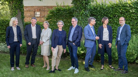 Gruppenfoto vom Rektorat der TU Dresden. Alle acht Rektoratsmitglieder stehen vor einer grünen Hecke auf einer Wiese und sprechen und lachen miteinander.